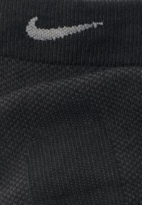 Μαύρες κάλτσες Nike με ριμπ υφή, που διαθέτουν γκρι κεντημένο λογότυπο. Το ύφασμα φαίνεται λείο και ελαστικό.