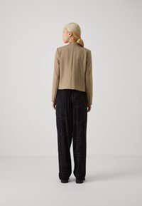 Beige fitted jacket with a high collar, paired with black loose-fit trousers featuring large white text patterns and elastic cuffs.