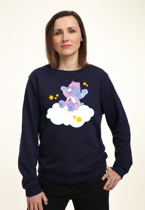 Marineblauwe sweatshirt met een afbeelding van een cartoonbeer op een wolk met gele sterren. Het ontwerp is kleurrijk, met zachte texturen en speelse elementen.
