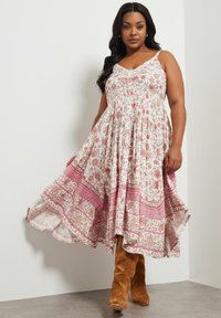 Vestido floral con base blanca, patrones rosas, escote en V y dobladillo acampanado. Combinado con botas de ante marrones hasta la rodilla.