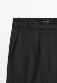 Pantaloni neri su misura con tasche laterali, passanti per cintura e un'etichetta Massimo Dutti visibile in vita, su sfondo bianco.