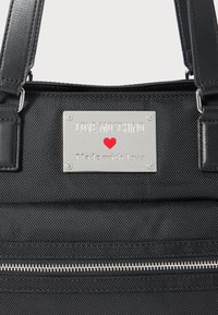 Black textured handbag with black leather straps and silver plate reading "LOVE MOSCHINO" with a red heart and "Made with love."