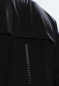 Schwarze wasserdichte Jacke mit einem eleganten, matten Finish, hohem Kragen, reflektierenden Akzentstreifen und minimalistischem Design.