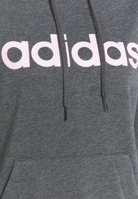 Szara bluza z kapturem, wykonana z miękkiego materiału, z przednią kieszenią i sznurkami do regulacji. Wyraźne białe logo "adidas" w pogrubionej czcionce na piersi.