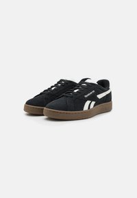 Zapatillas de ante negro con un acabado texturizado, franja lateral blanca y suela de goma marrón. Tienen punta redonda y diseño con cordones.