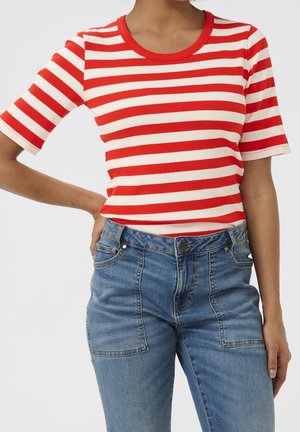 Vrouw draagt een rood-wit horizontaal gestreept T-shirt met korte mouwen, ingestopt in een high-waisted blauwe spijkerbroek met grote voorzakken.