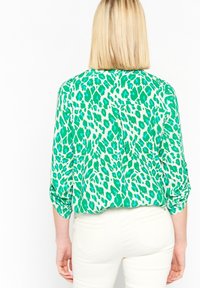 Green and white leopard print blouse with roll-up sleeves, featuring a back yoke detail and a single rear pocket. Made of lightweight fabric.