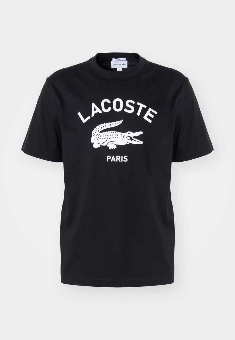 T-shirt noir à manches courtes avec un logo blanc Lacoste, représentant un crocodile à la bouche ouverte et le mot Paris en dessous.