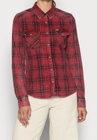 Camisa de cuadros roja y negra con mangas largas, dos bolsillos en el pecho, cierre de botones y dobladillo curvado. Hecha de un tejido suave y ligero.