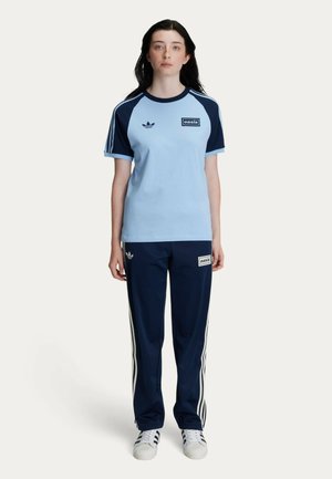 Light blue cotton t-shirt with navy raglan sleeves, featuring white stripes and an "oasis" logo. Paired with navy track pants with white stripes.
