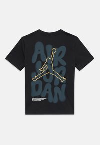 Camiseta negra con gran texto azul "AIR JORDAN", logo Jumpman contorneado en amarillo y pequeño texto blanco que dice "Productos inspirados en el mejor jugador de todos los tiempos."