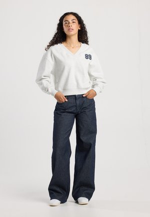 Lichtgrijze V-hals sweatshirt met geribbelde manchetten en een donkerblauwe '89'-print op de linkerborst, gecombineerd met brede, marineblauwe gestreepte broeken.