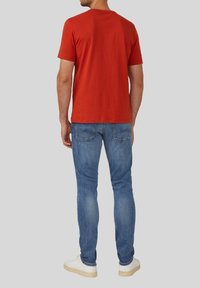 Rood T-shirt met korte mouwen, gemaakt van katoen, gecombineerd met blauwe slim-fit jeans en witte sneakers. Zichtbare stiksels op de jeans.