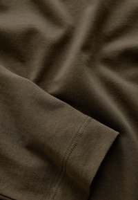 Primo piano di tessuto verde oliva che mostra una manica piegata con cuciture visibili e una texture morbida.