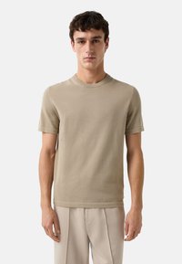 Pull en tricot beige à manches courtes avec un col ras du cou et une texture subtile, associé à un pantalon ample de couleur claire.