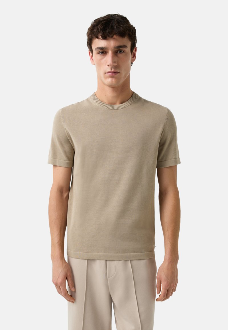 Pull en tricot beige à manches courtes avec un col ras du cou et une texture subtile, associé à un pantalon ample de couleur claire.