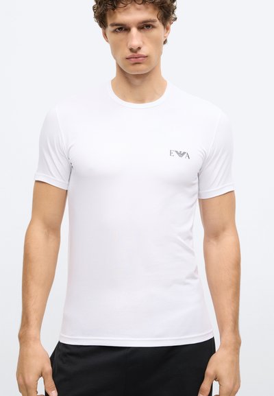 Balta īsroku kokvilnas T-krekls ar mazu melnu logotipu kreisajā krūšu daļā. Klasisks apaļš kakla izgriezums, pieguļošs dizains.