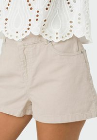 Shorts en velours côtelé beige clair avec une surface texturée, dotés de poches avant et d'une fermeture à bouton en métal. Coupe ajustée au niveau de la taille.