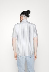 Camicia a maniche corte di colore bianco con righe verticali grigie. Presenta un colletto e un orlo dritto. Il materiale sembra leggero e dalla texture interessante.