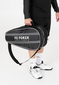 Mustapohjainen urheilulaukku valkoisilla yksityiskohdilla ja "FZ FORZA" -logolla, jossa on tyylikäs, pitkä muotoilu, pehmustettu olkahihna ja vetoketjukiinnitys.