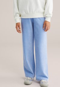 Gaiši zili korduroja platā stila bikses ar vertikālu ribu, kombinētas ar baltu sporta krekli. Gluda tekstūra un brīvs griezums.