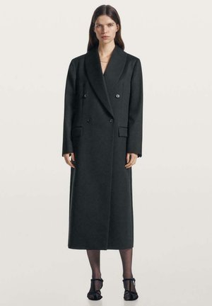 Cappotto doppiopetto in lana grigio scuro con ampi revers, tasche laterali e vestibilità sagomata, che arriva a metà polpaccio. La silhouette è strutturata.