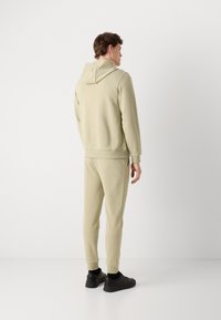 Felpa beige chiaro e pantaloni jogger abbinati in un morbido tessuto. Presenta un piccolo cappuccio e polsini a coste; indossati con sneakers nere.