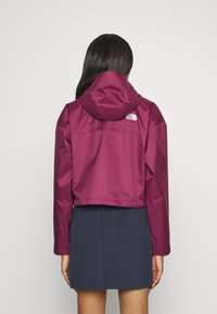 Przycięta bordowa kurtka z kapturem i logo The North Face na plecach, połączona z granatową spódnicą z dwoma tylnymi kieszeniami.