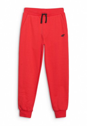 Chłopiec stoi z rękami w kieszeniach, ubrany w czarną koszulkę z logo 4F, czerwone spodnie dresowe i czarne buty sportowe na jednolitym tle.