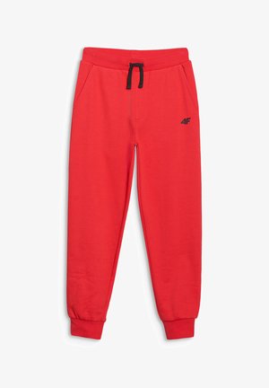 Chłopiec stoi z rękami w kieszeniach, ubrany w czarną koszulkę z logo 4F, czerwone spodnie dresowe i czarne buty sportowe na jednolitym tle.