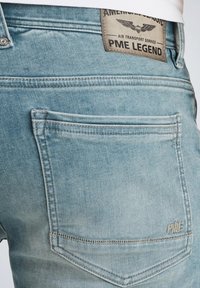 Jeans de denim azul claro con un acabado desgastado, con un bolsillo trasero y una etiqueta de cuero rectangular que dice "PME Legend."