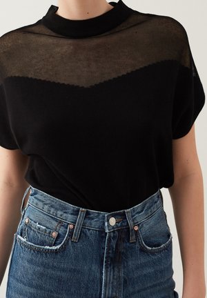 Haut noir à manches courtes avec empiècement en résille transparente et col rond, associé à un jean en denim bleu taille haute avec bords des poches effilochés.