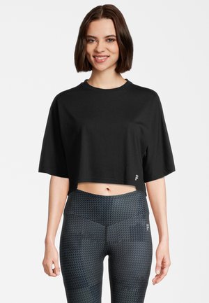 T-shirt atletico nero, corto, con maniche corte e collo rotondo, abbinato a leggings scuri con una fantasia a motivi geometrici sottili.