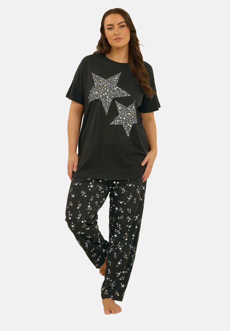 Top nero a maniche corte con design di stelle argento e oro; pantaloni da pijama neri con piccoli motivi di stelle bianche e oro.