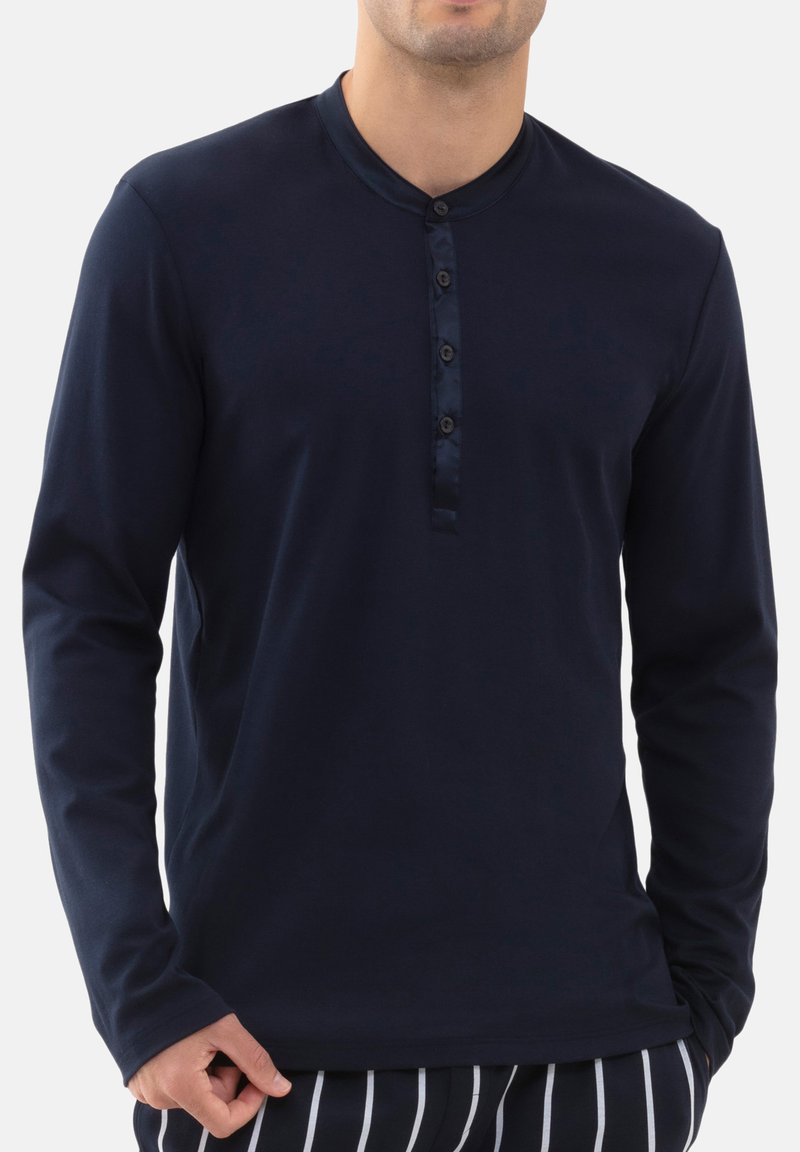 Camicia a maniche lunghe di colore blu navy con una texture liscia, apertura con bottoni e design del colletto rotondo. Abbinata a pantaloni a righe.