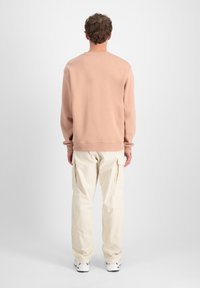 Felpa rosa pallido con polsini e orlo a costine, abbinata a pantaloni cargo beige a gamba larga con tasche laterali.