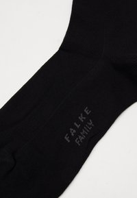 Chaussette noire avec une texture côtelée, présentant un discret logo "FALKE FAMILY" en gris sur le côté. Design élégant et ajusté.
