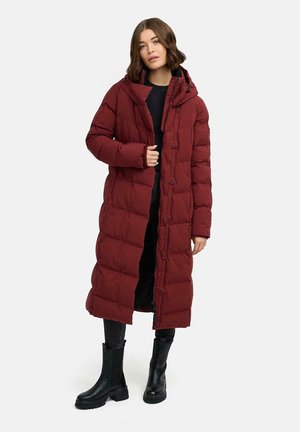 Bordeaux gewatteerde jas met een georganiseerd gestikt ontwerp, een capuchon en knoopsluiting. Gecombineerd met zwarte broek en zwarte laarzen tot de knie.