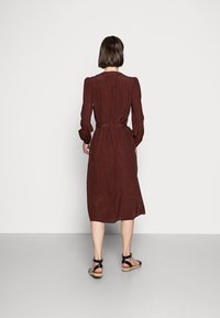 Vestito lungo con cintura a maniche lunghe di un colore rosso scuro con un motivo sottile, gonna fino al ginocchio e tessuto morbido; abbinato a sandali neri con cinturini.
