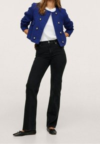 Blauwe textuur jas met gouden knopen, witte blouse, zwarte wijde jeans en zwarte platte schoenen. Benadrukt een getailleerd silhouet en casual stijl.