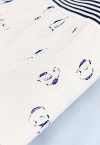 Tessuto in cotone con uno sfondo bianco decorato da motivi stampati blu navy. Un bordo a righe blu navy e bianco è visibile.