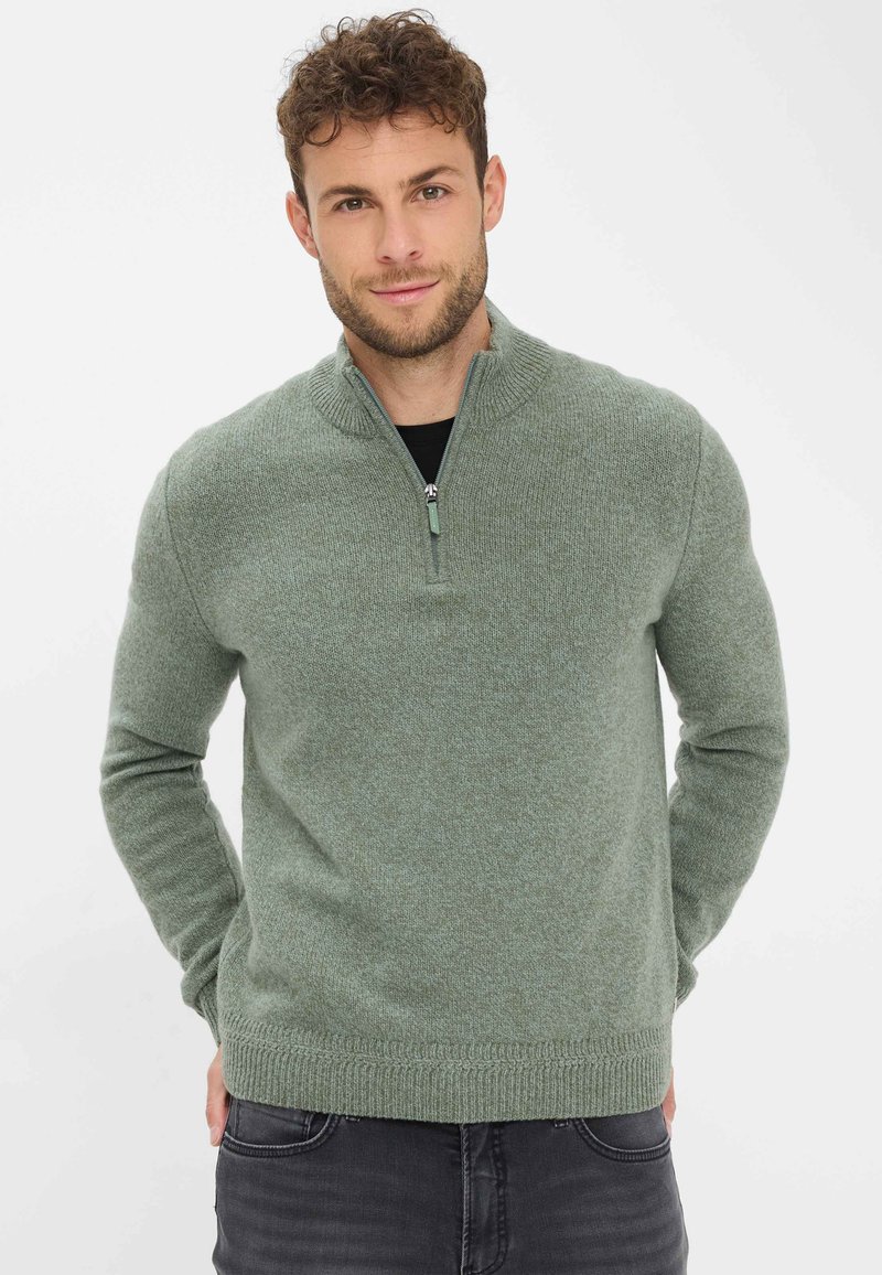 Hellgrüner Zip-Kragen-Pullover aus strukturiertem Strickstoff mit langen Ärmeln, gerippten Bündchen und Saum, kombiniert mit dunklen Jeans.