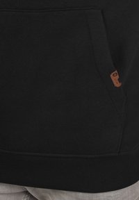 Zwarte sweatshirt met een voorkantzak, voorzien van een klein bruin leren label. Ribbelboord aan de onderkant en mouwen. Glad materiaal.