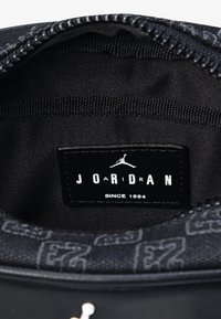 Čierny interiér tenisky Jordan s textúrovaným podšívkou, s etikettou, na ktorej je nápis "J O A R D A N" a "SINCE 1984" v bielej farbe.