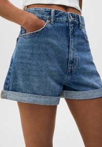 Jeansshorts i mellanblått med en något bleknad finish, försedda med upprullade fållar, framfickor och kopparfärgad metall.