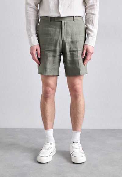 Olive green linen shorts with a tailored fit, side pockets, and a smooth texture, paired with white sneakers and ankle-length socks.