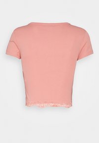 Krátký růžový cropped tričko s kulatým výstřihem a krátkými rukávy, se zdobným krajkovým lemem na spodním okraji. Měkká bavlněná tkanina.