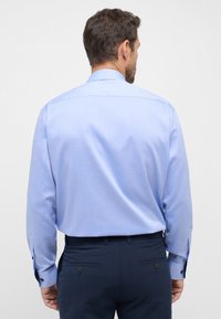 Lichtblauw langslijf shirt met een button-down kraag, een soepele textuur en contrasterende donkere knopen op de manchetten, gecombineerd met donkerblauwe broek.