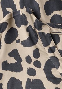 Tissu à motifs animaliers présentant de grandes taches de léopard gris foncé sur un fond beige. Surface texturée avec des détails de couture visibles.