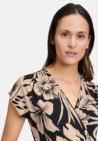 Haut à motifs floraux noir et beige avec un design en V, des manches courtes, et une texture en tissu doux, mettant en valeur de grands motifs de fleurs tropicales.